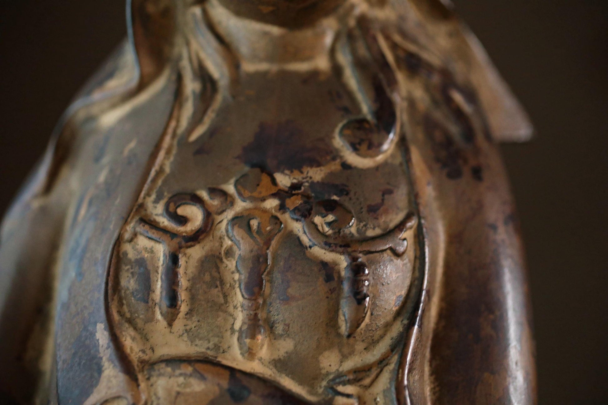 a close-up view of a bronze statue or sculpture, with intricate details and patterns visible.