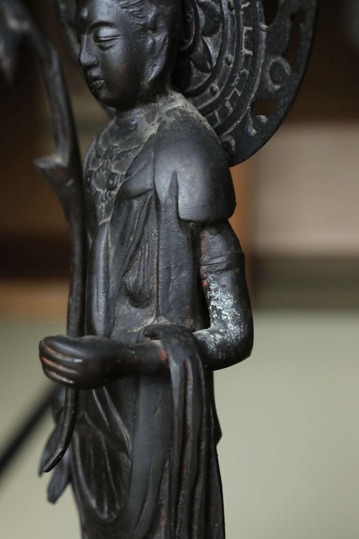 A close-up view of a black metal statue depicting a figure with a flowing robe and a large headdress.