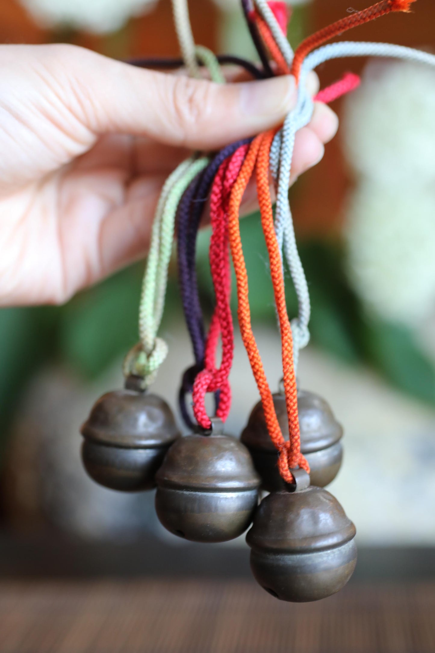 A hand is holding a bunch of colorful metal bells, with the bells hanging from strings.