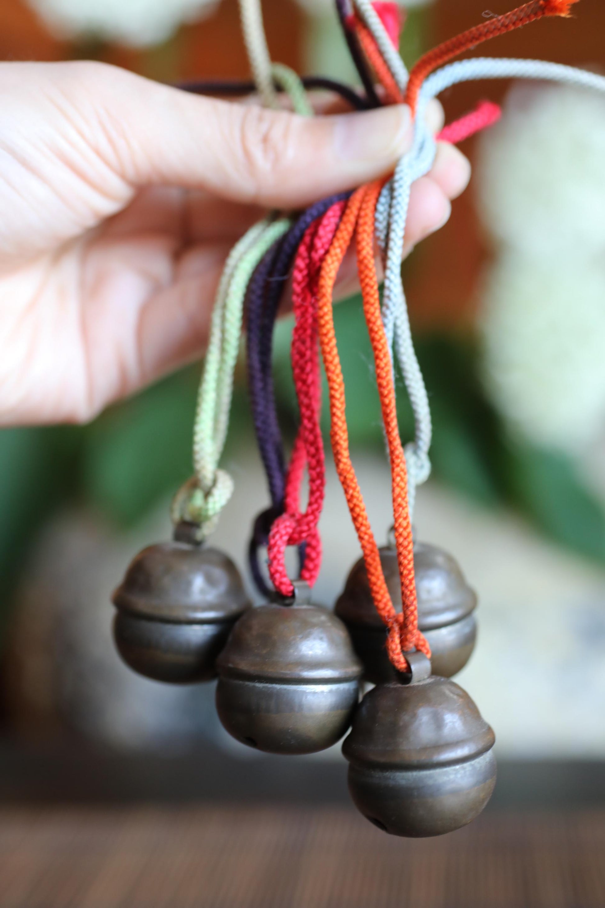 A hand is holding a bunch of colorful metal bells, with the bells hanging from strings.