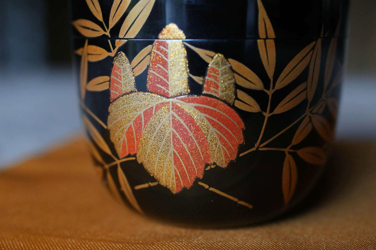 A close-up view of a decorative ceramic container with a black background and gold leaf-like patterns.