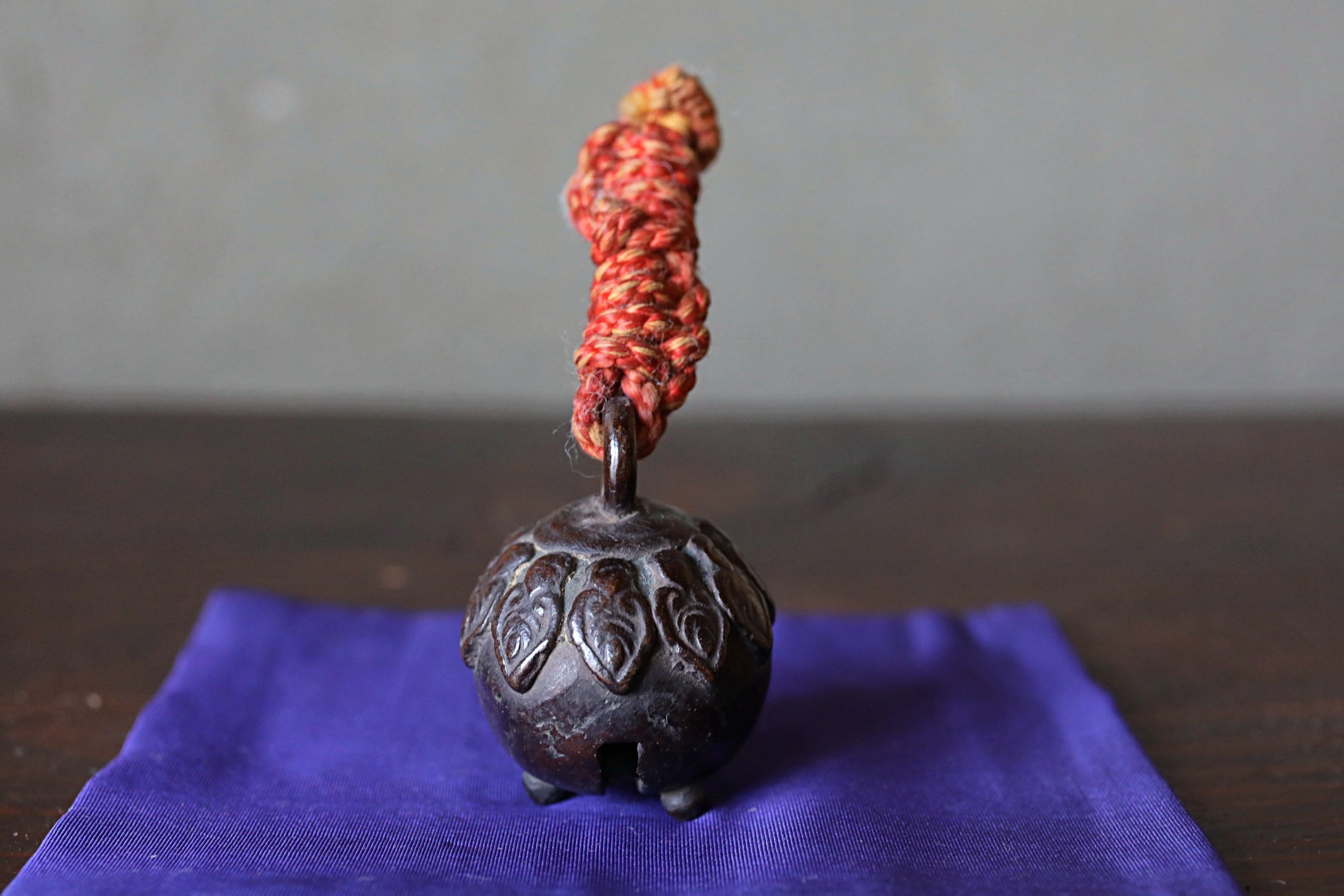 A small, round, metal bell with a red and yellow rope or string attached to it, placed on a blue cloth or napkin.