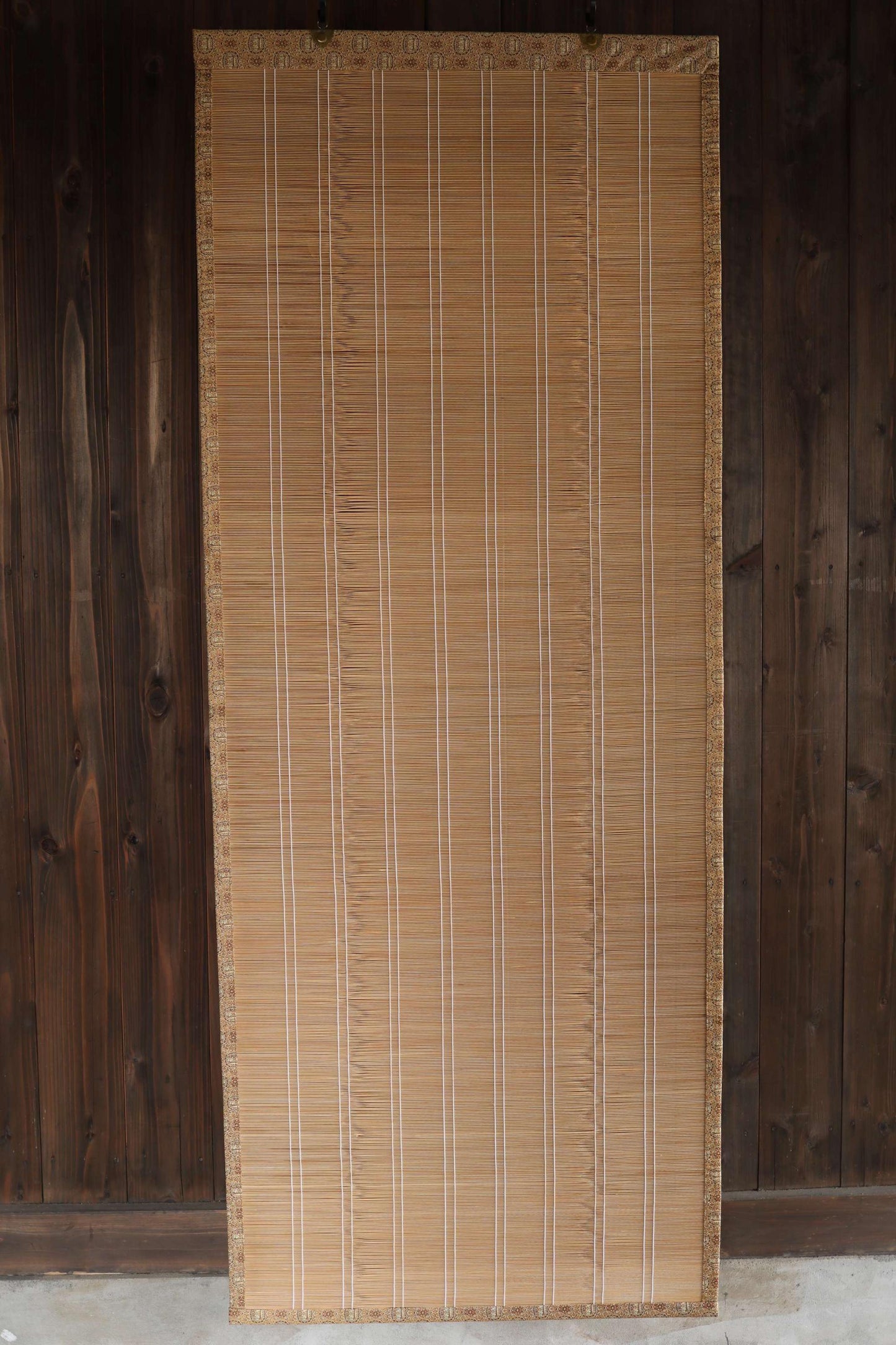 a bamboo screen or blind with vertical slats, placed against a wooden wall.