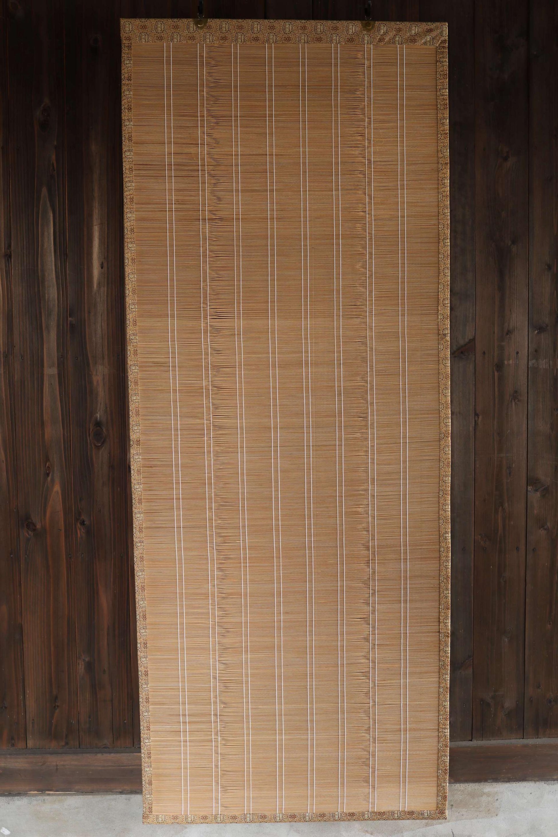 a bamboo screen or blind with vertical slats, placed against a wooden wall.