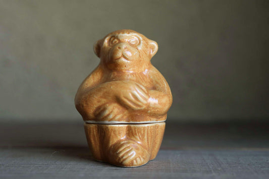 A ceramic figurine of a monkey sitting on a wooden base.