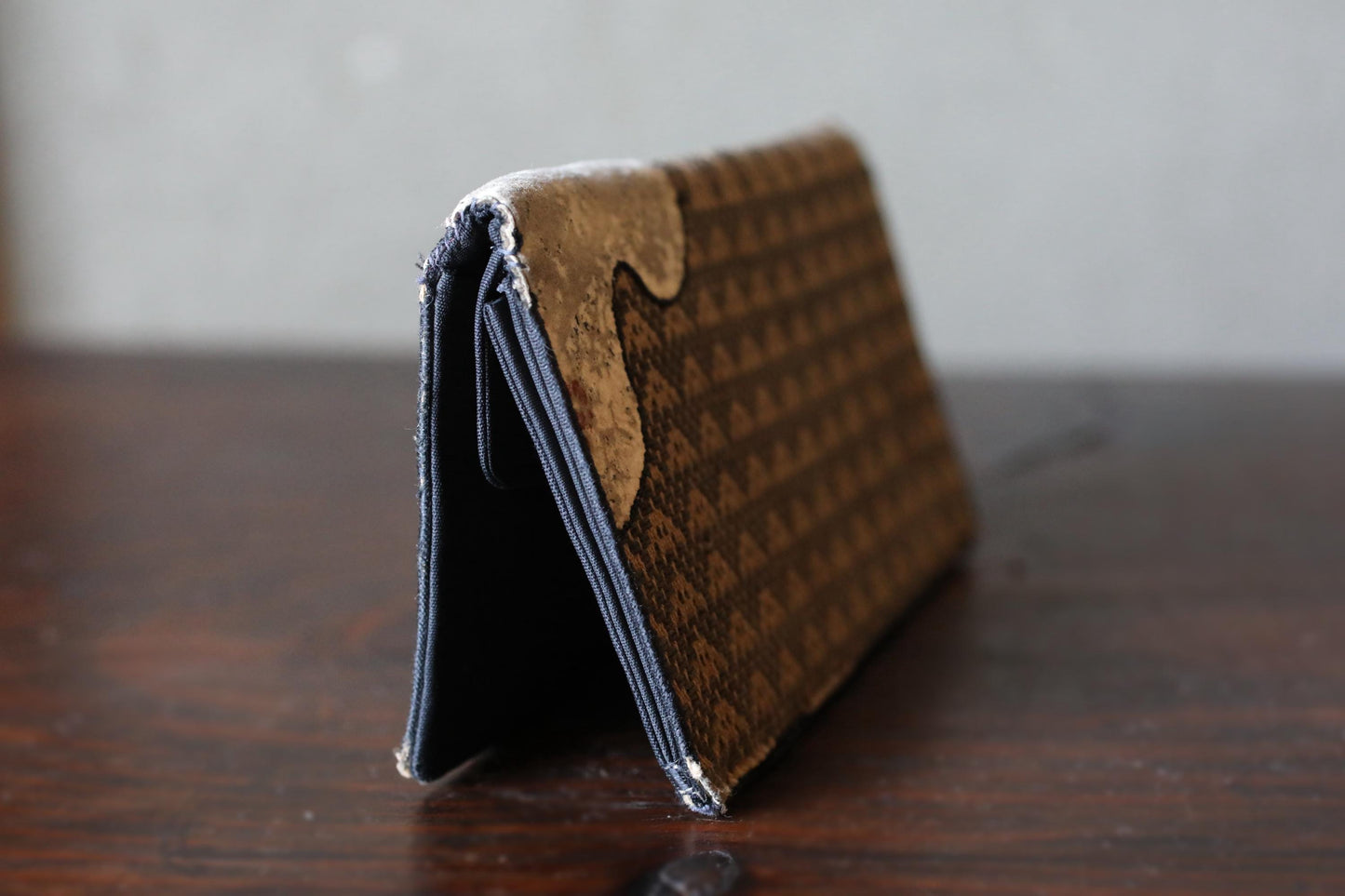 A brown wallet with a patterned design sits on a wooden surface.