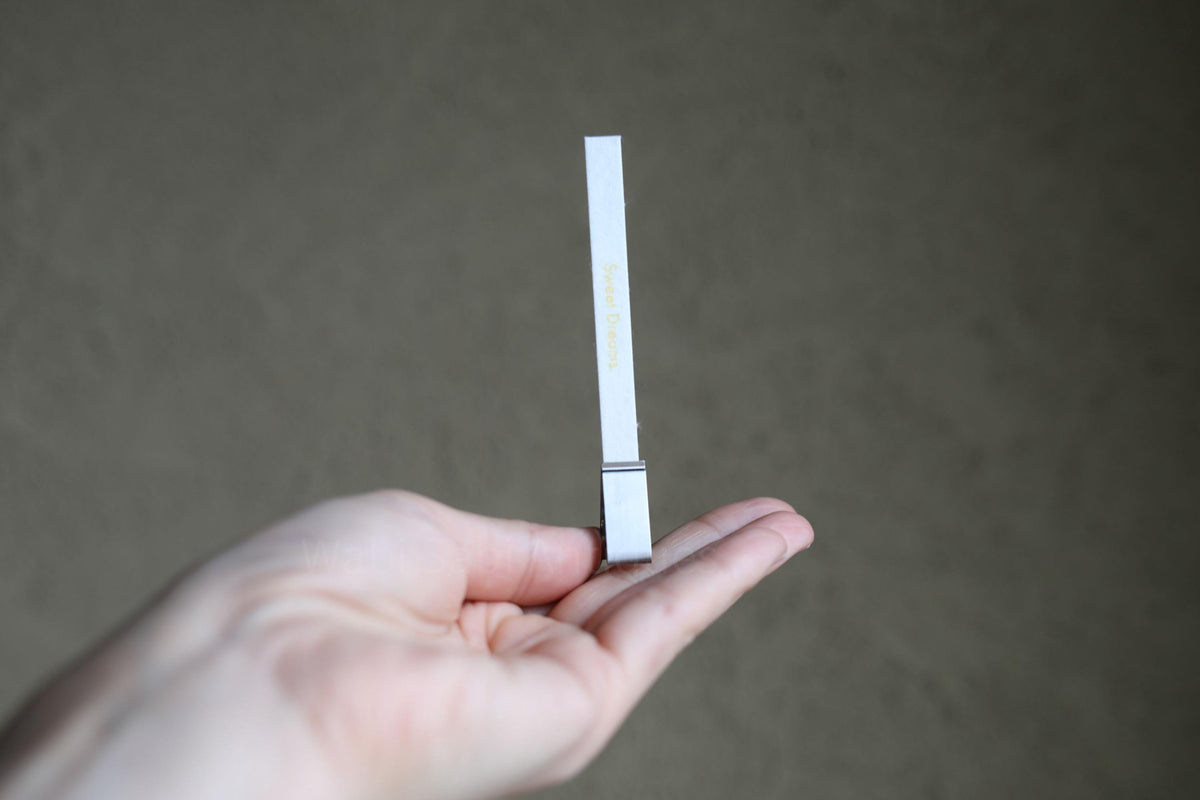 A hand holding a small white object, which appears to be a paper clip, against a grey background.