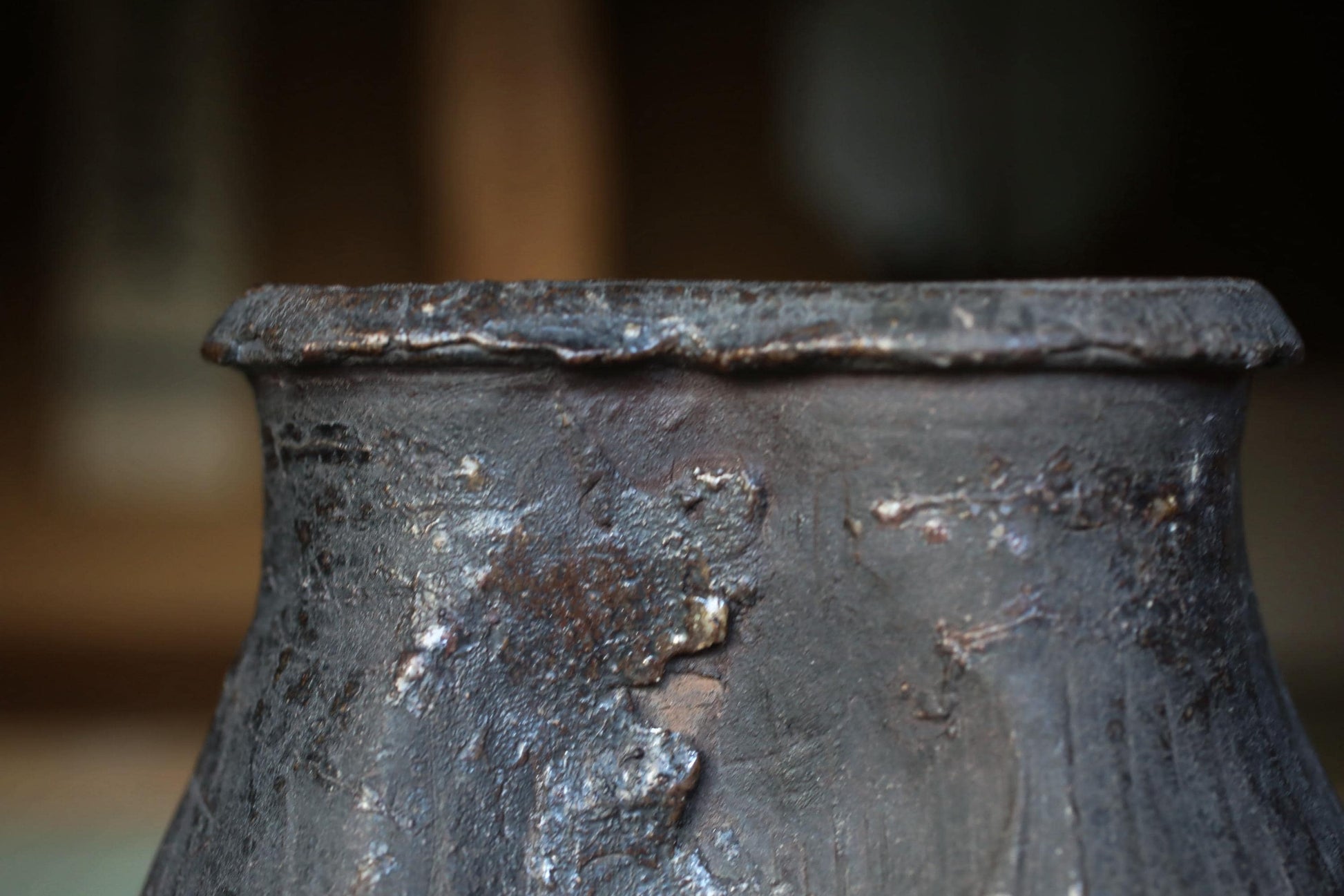 A close-up view of a dark, textured metal object, possibly a piece of pottery or a sculpture, with a blurred background.