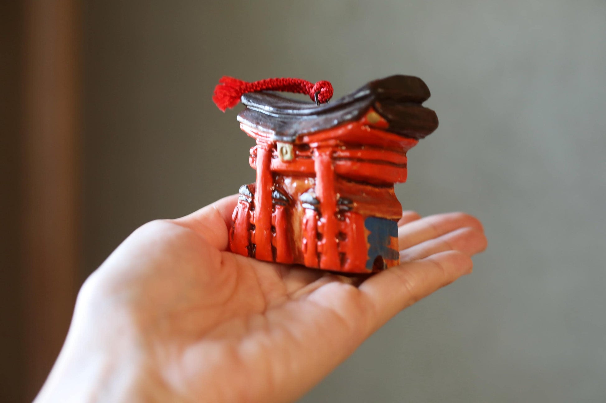 A hand holding a small, red figurine of a temple or shrine with a red tassel on top.