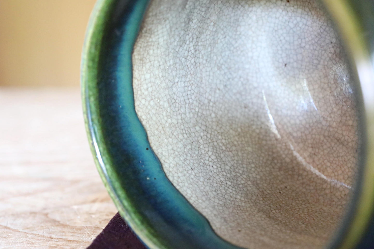 A close-up view of a ceramic bowl with a green rim and a white interior, resting on a wooden surface.