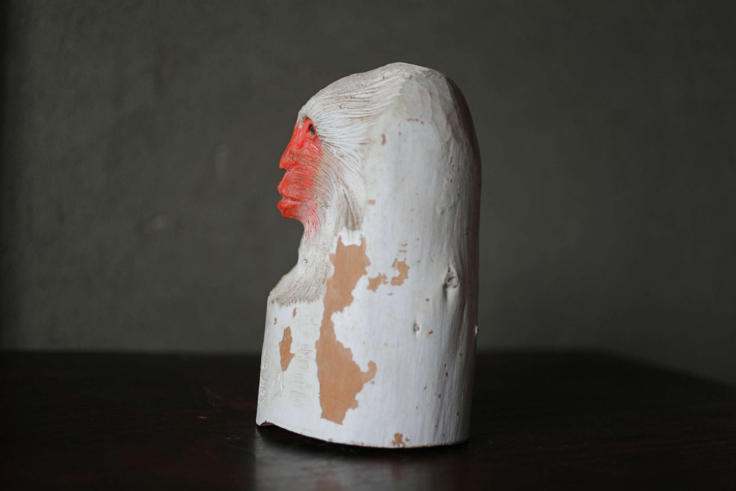 A white wooden sculpture with red markings on its surface, sitting on a dark surface.