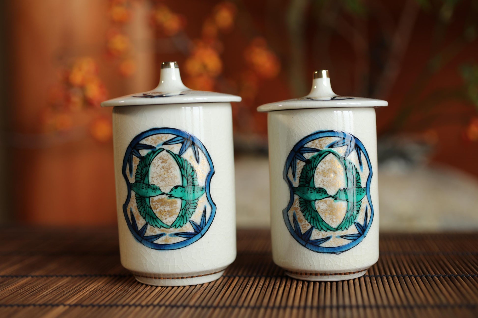 Two white ceramic jars with blue and green designs on them, placed on a wooden surface.