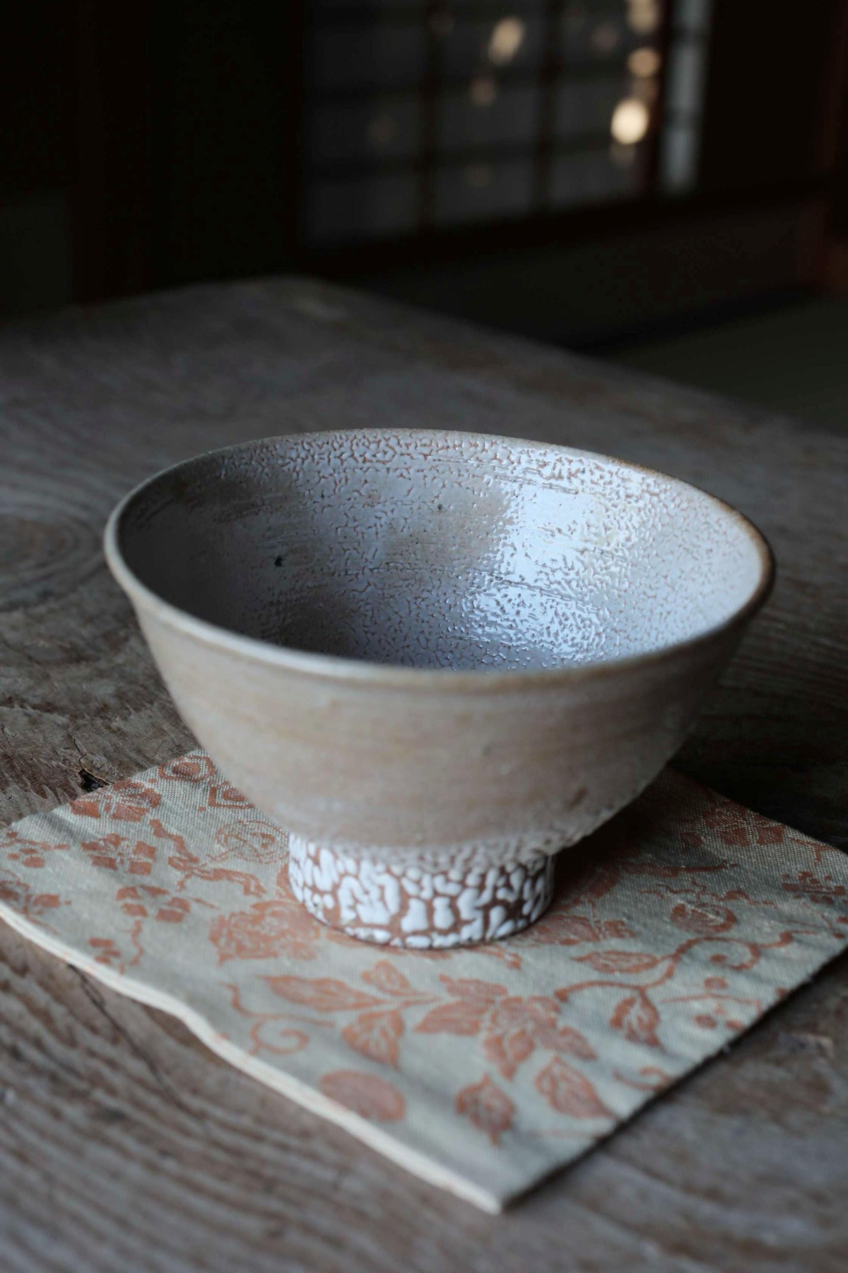 A white ceramic bowl with a textured surface sits on a wooden surface, with a floral patterned napkin underneath.