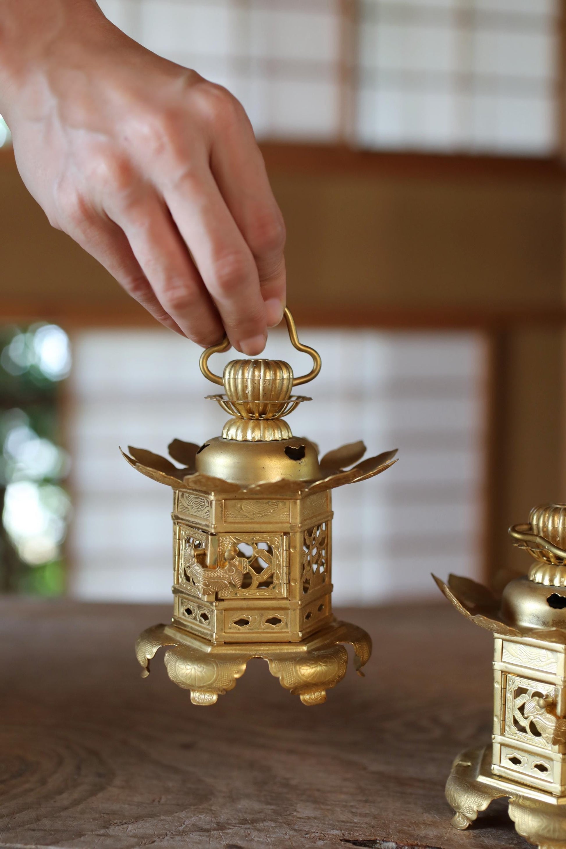 A hand is holding a golden lantern with intricate designs on a wooden surface.