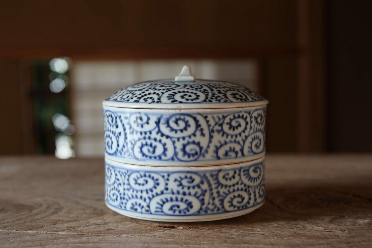 A decorative blue and white ceramic container with a lid sits on a wooden surface.