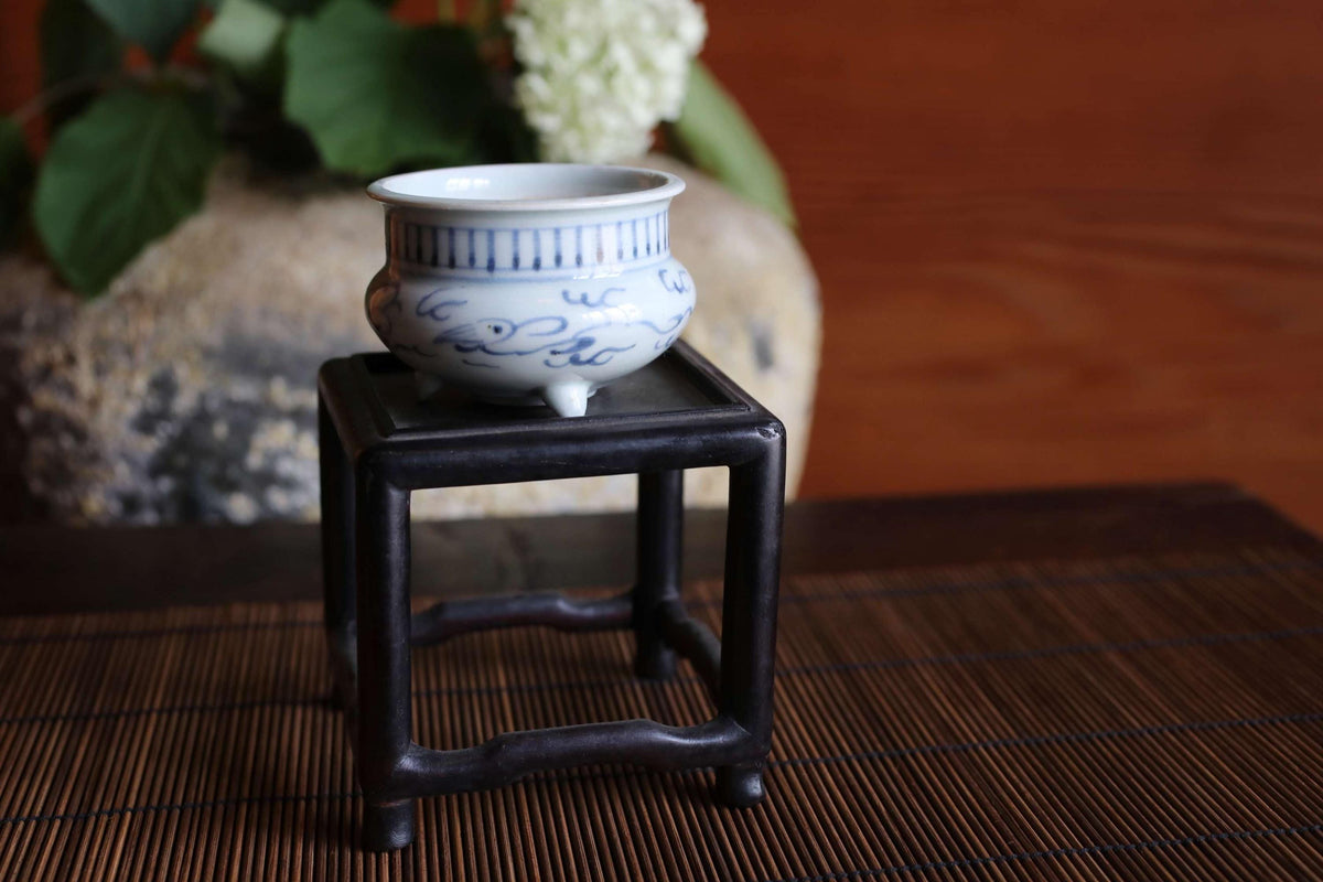 A small blue and white ceramic bowl is placed on a black metal stand on a bamboo mat.