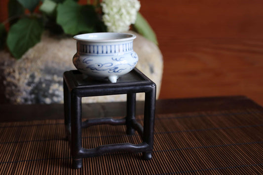 A small blue and white ceramic bowl is placed on a black metal stand on a bamboo mat.