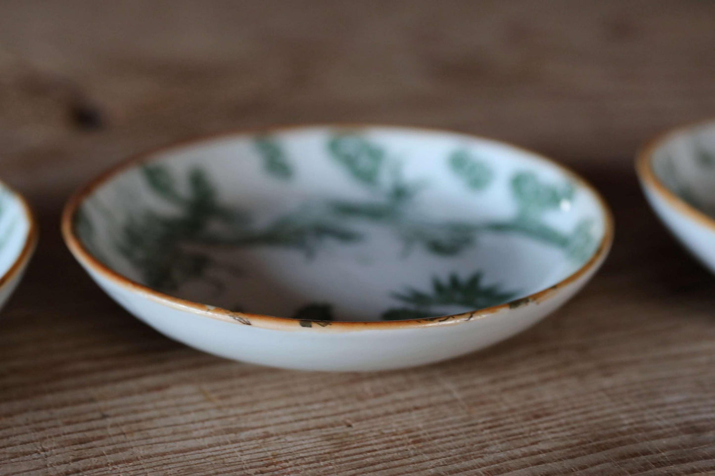 A white bowl with a green floral pattern sits on a wooden surface.