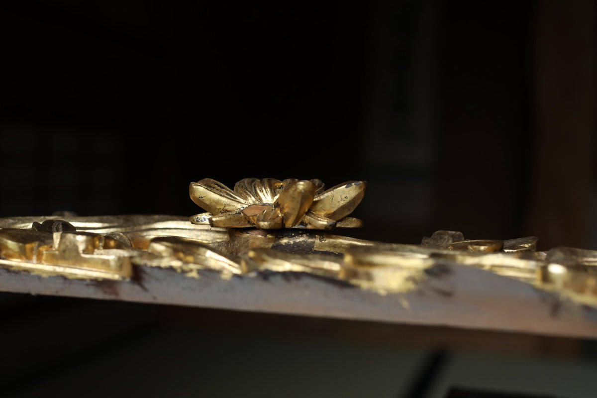 a close-up view of a golden, ornate object with intricate details, such as a flower or leaf-like design, resting on a surface.