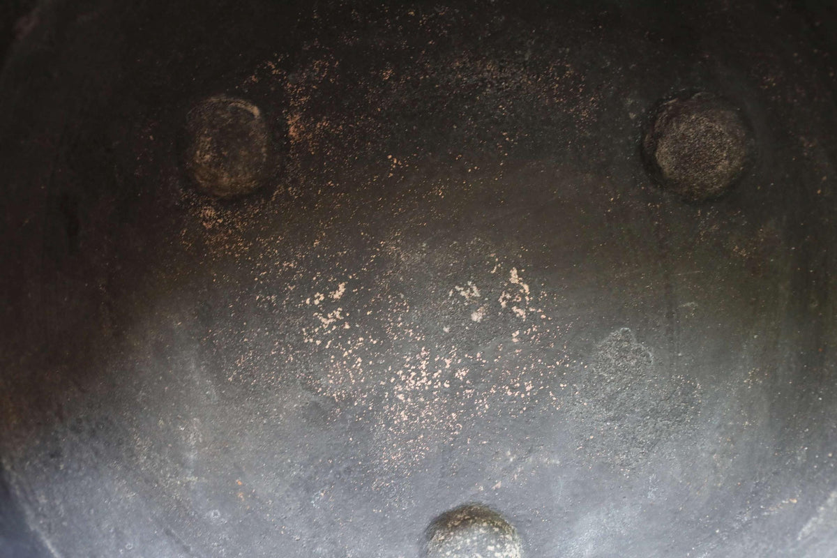 a close-up view of a black, rusted metal surface with three circular holes, likely made of iron or steel. The surface appears to be dirty and worn, with patches of rust visible on the surface.