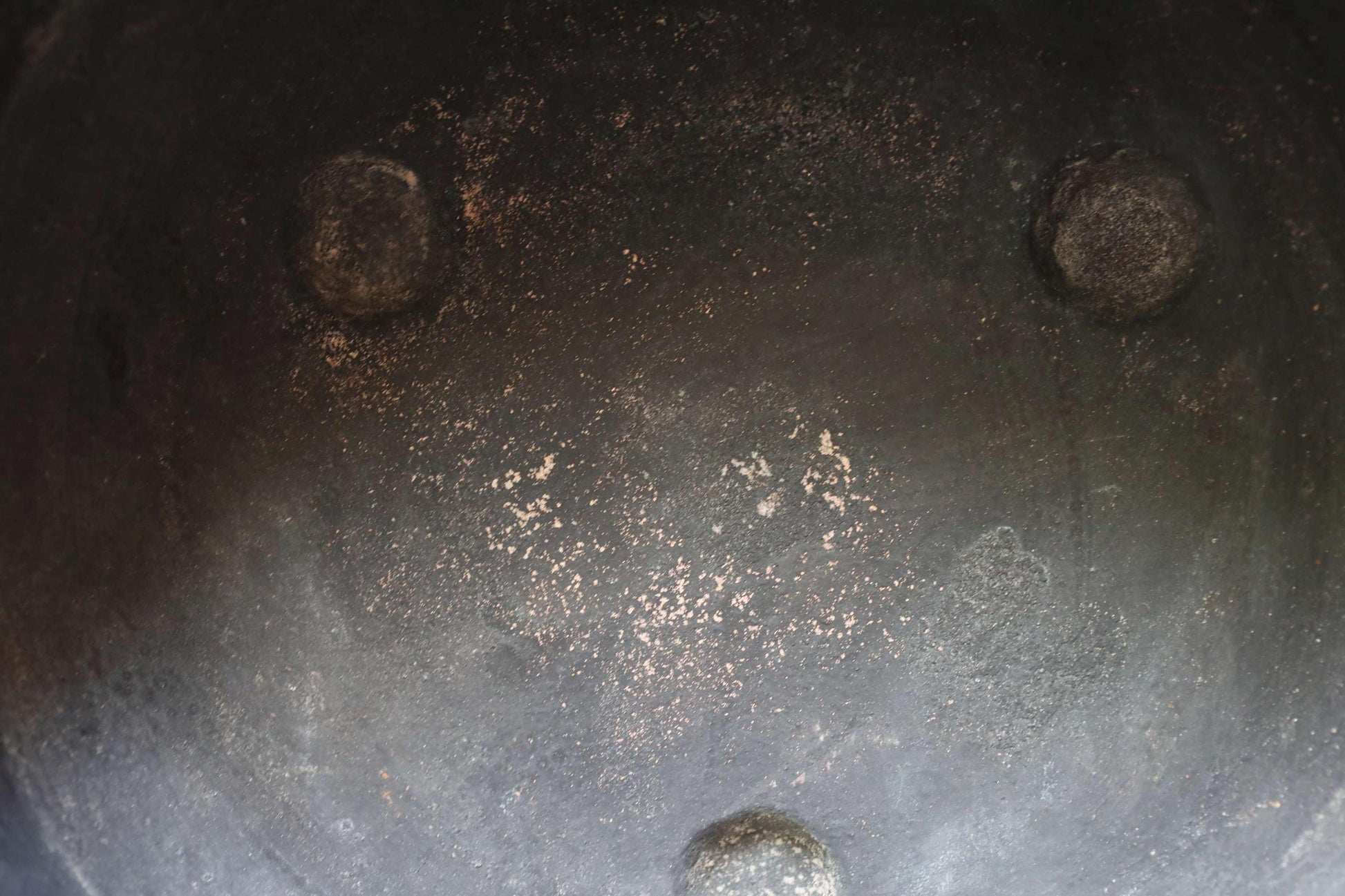 a close-up view of a black, rusted metal surface with three circular holes, likely made of iron or steel. The surface appears to be dirty and worn, with patches of rust visible on the surface.