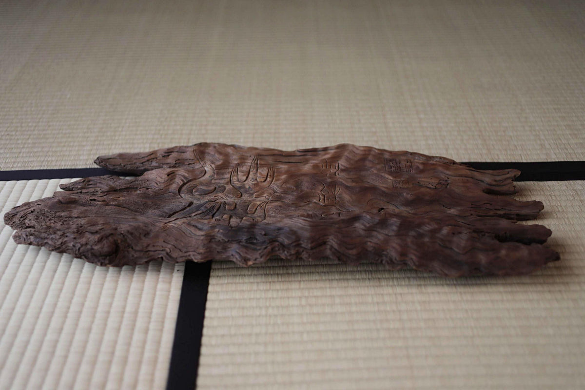 a piece of driftwood with a carved design on its surface, resting on a white mat with black lines.