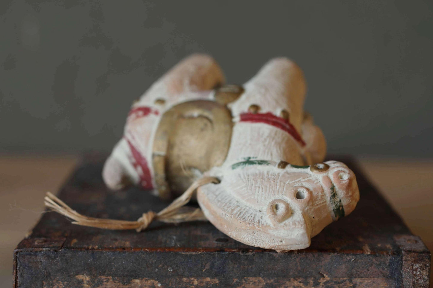 A close-up image of a small, white ceramic figurine with red and green accents, sitting on a wooden surface.