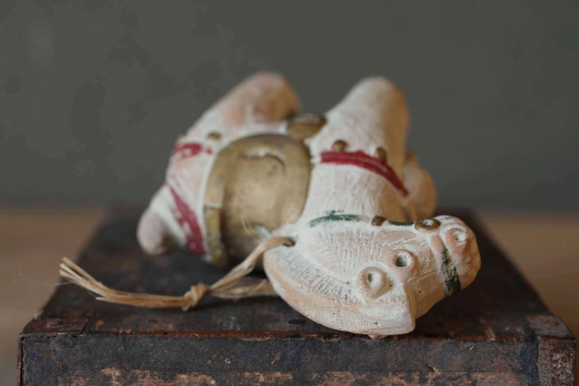 A close-up image of a small, white ceramic figurine with red and green accents, sitting on a wooden surface.