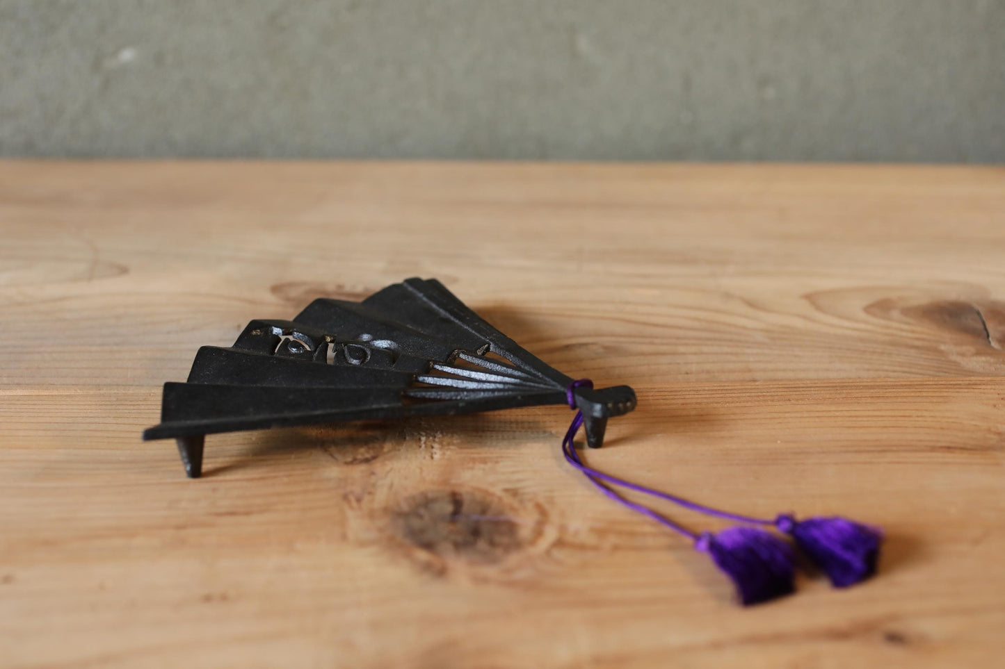 A black metal fan with purple tassels is placed on a wooden surface.