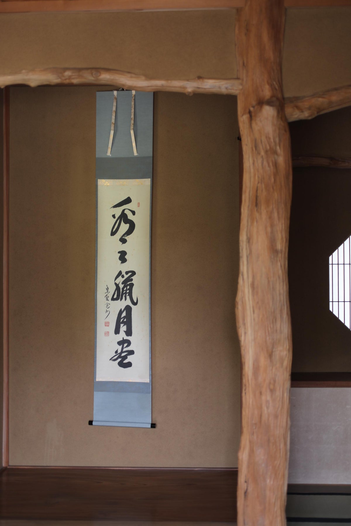 a wooden beam with a vertical scroll hanging on the wall, displaying Japanese characters.