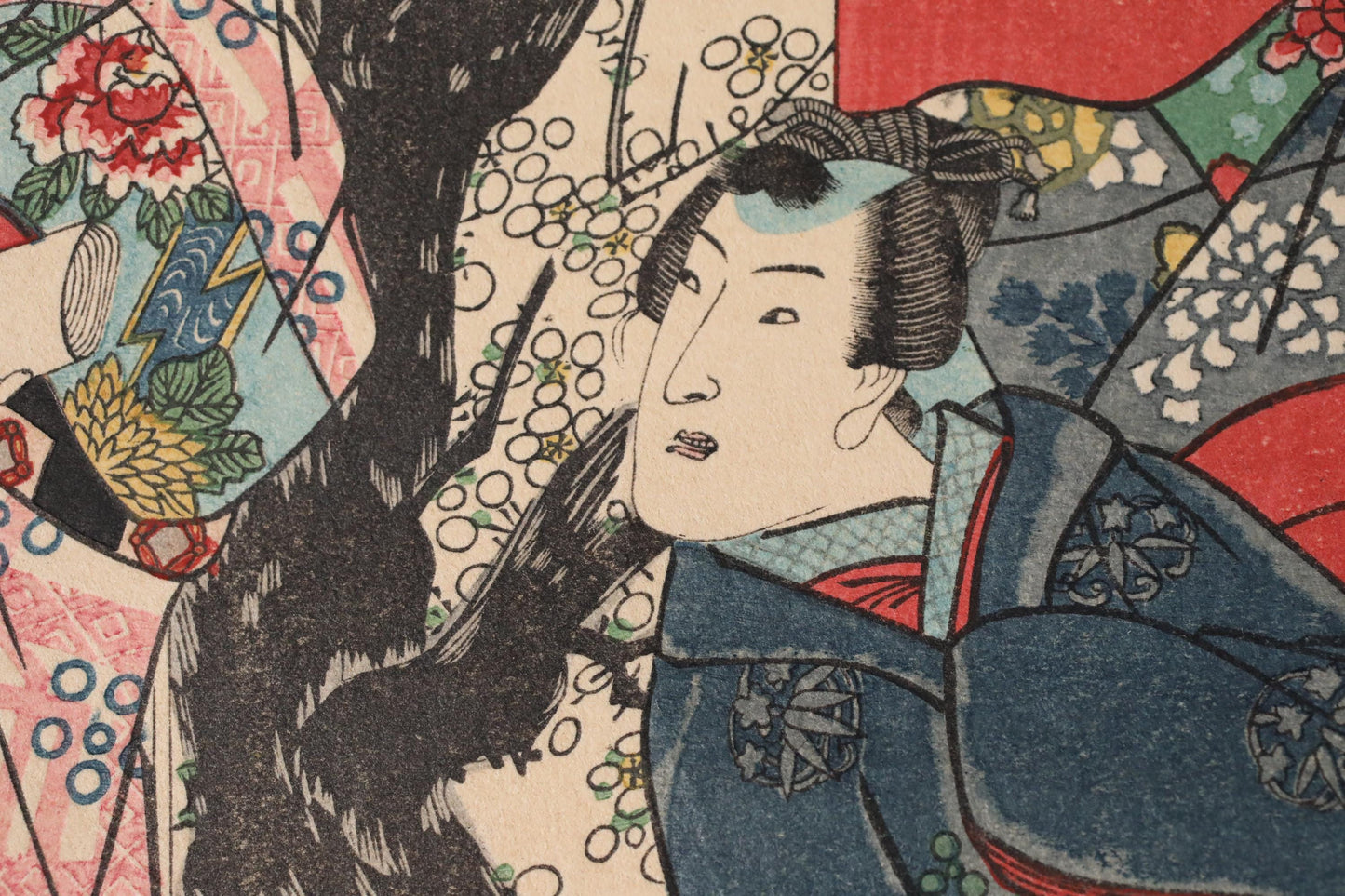 The image is a close-up of a detailed Japanese woodblock print featuring a woman with an intricate hairstyle and a colorful, patterned background.