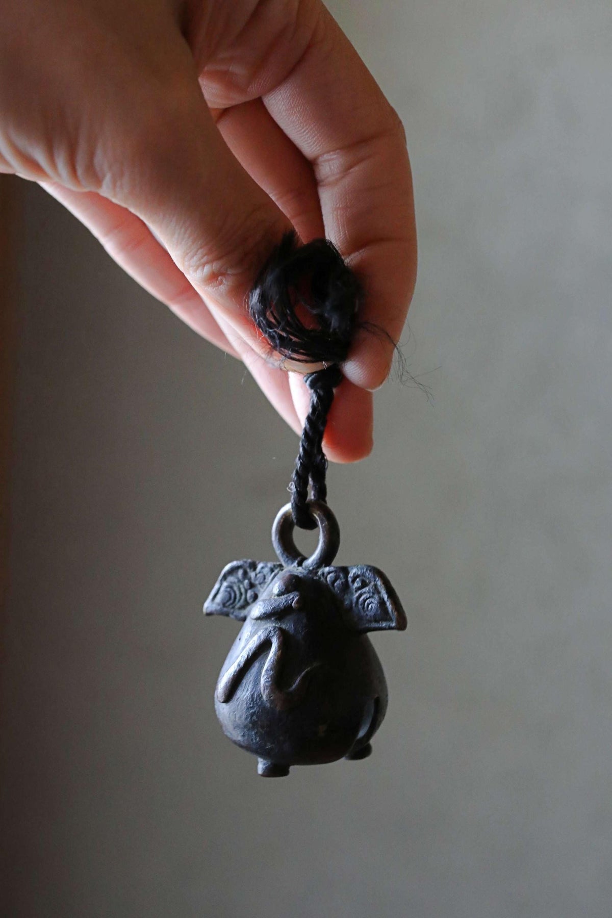 A hand is holding a small, black metal bell with a rope attached to it.