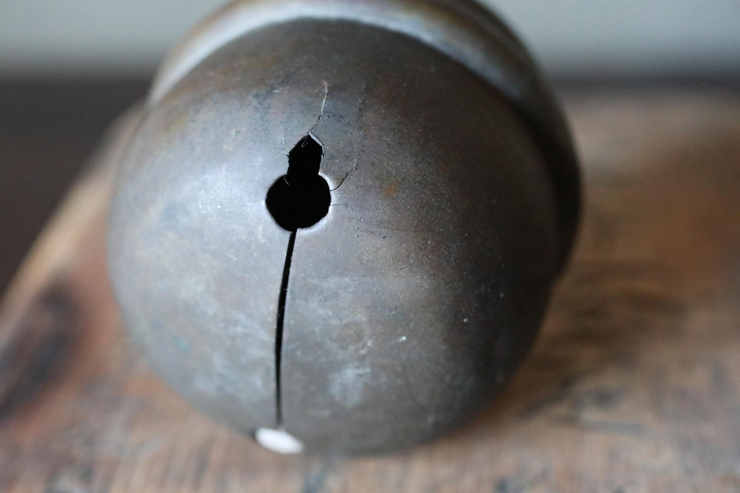 A close-up image of a metal bell with a hole in the center, resting on a wooden surface.