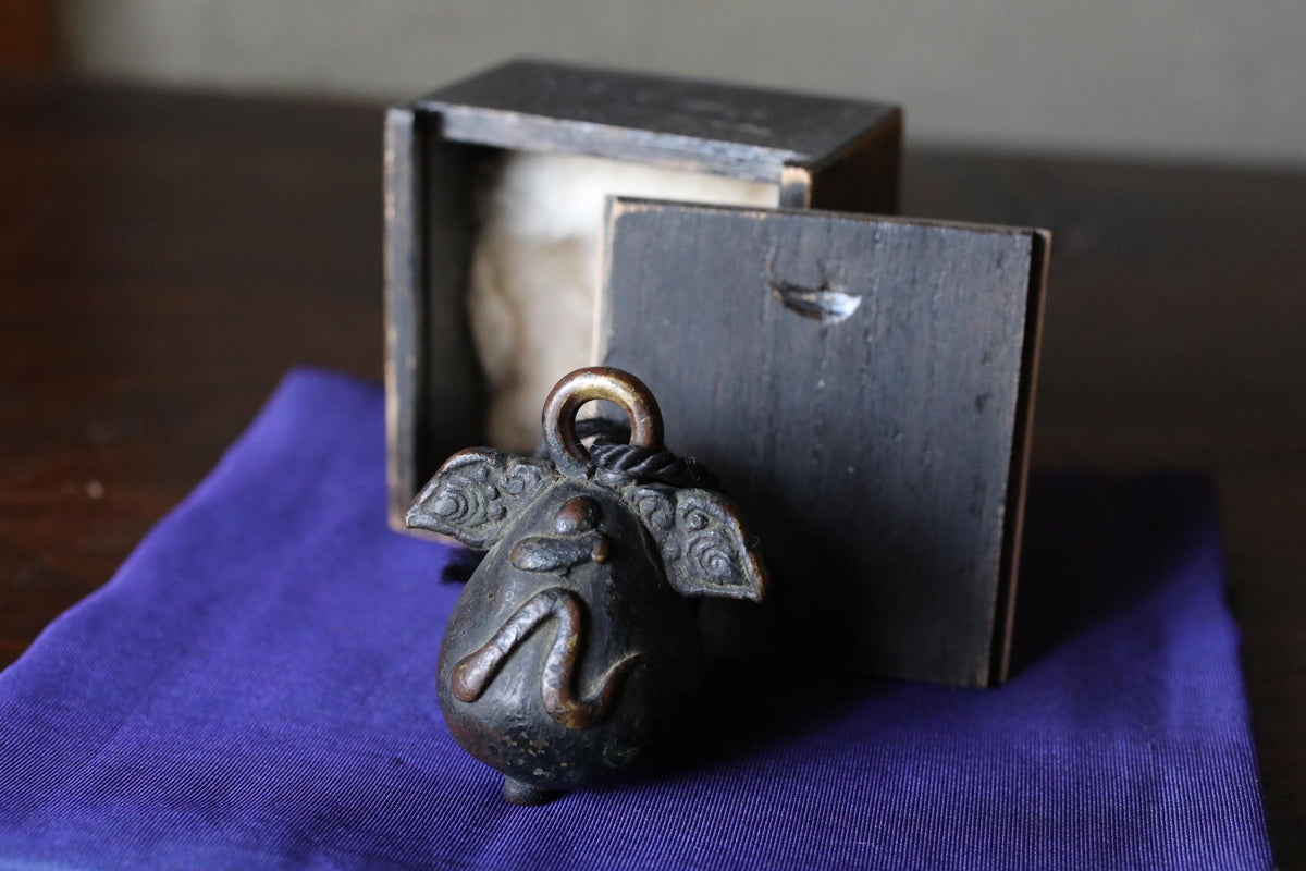 a small, ornate metal bell with a dark, textured surface, placed on a blue cloth.