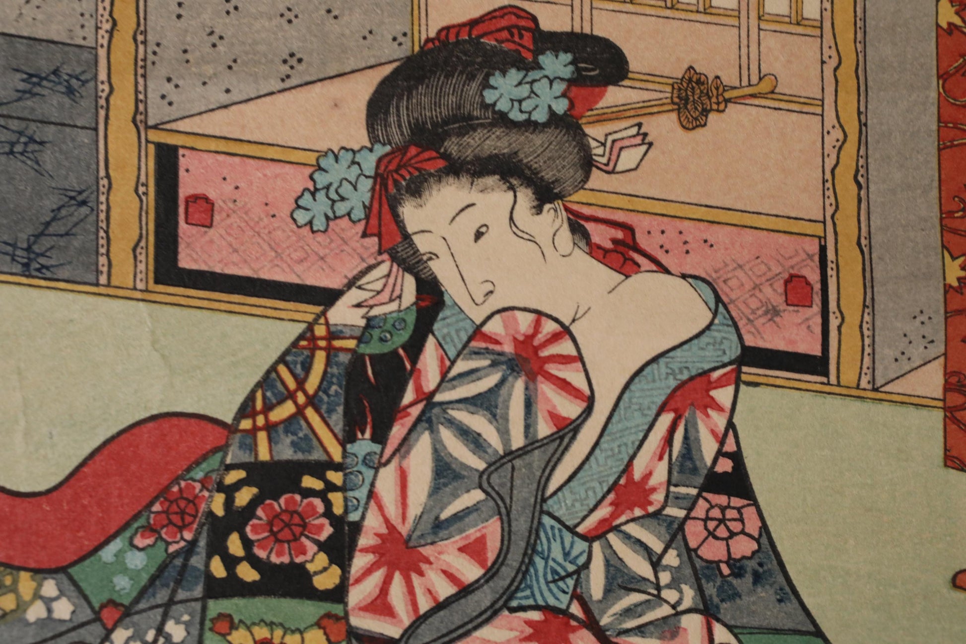 A close-up of a woman wearing a colorful, patterned kimono with a floral headpiece, sitting in a room with a window and other decorative elements.