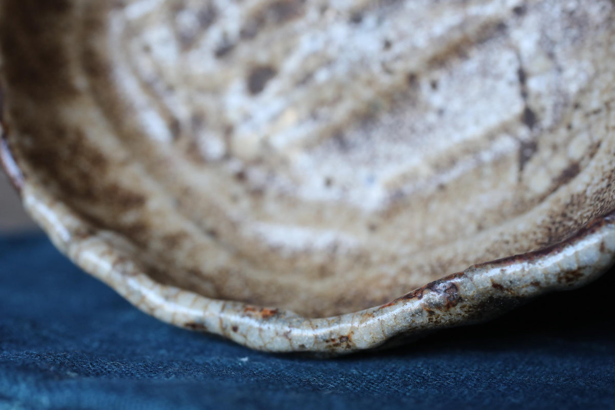 A close-up view of a ceramic bowl with a textured surface, resting on a blue fabric background.