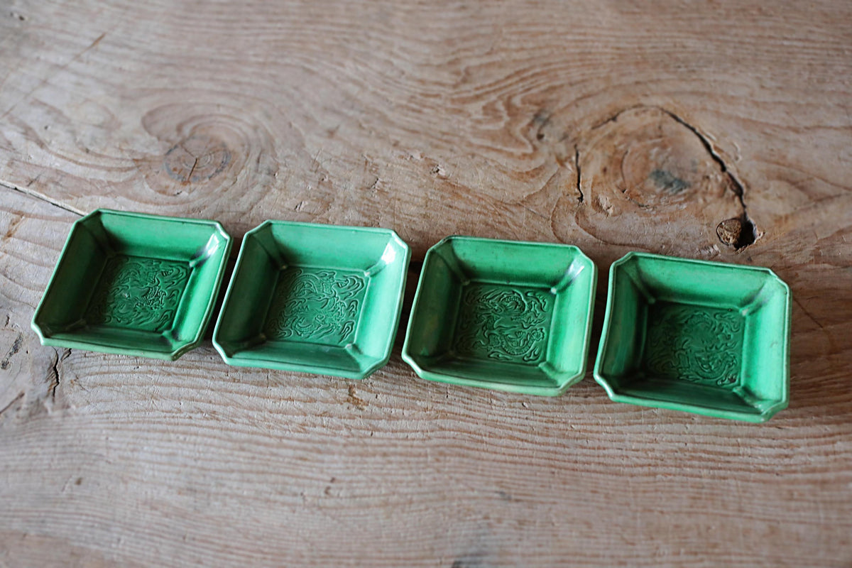 Four green square bowls arranged in a row on a wooden surface.