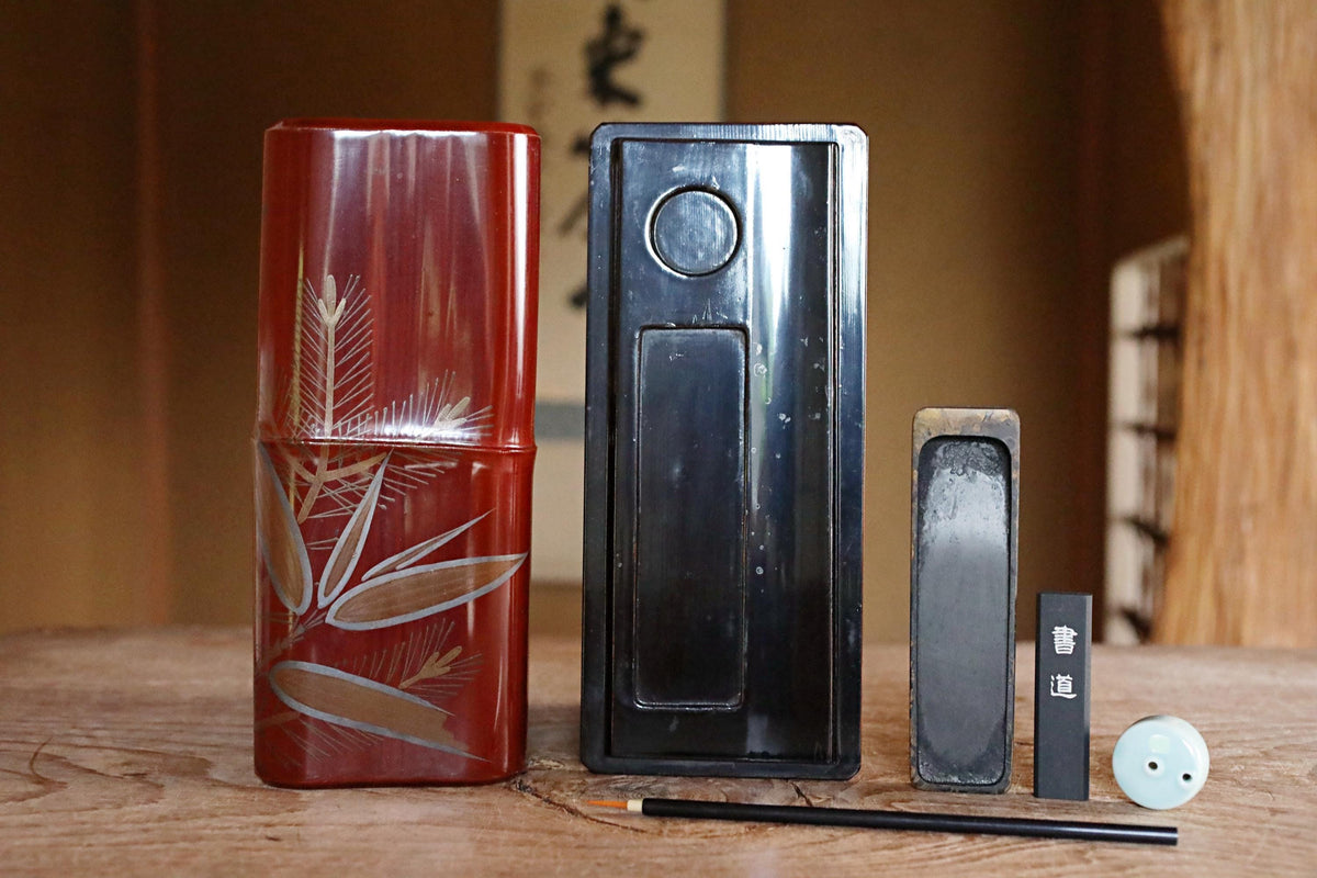 a wooden table with various objects, including a red vase with a leaf design, a black rectangular object, a small black object, and a white object.