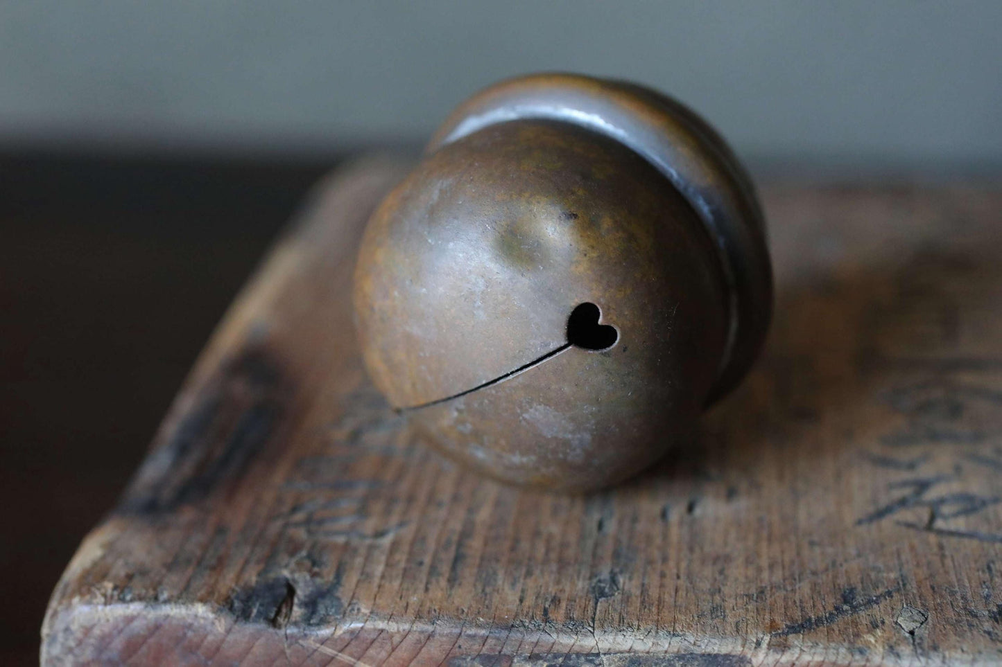 An old, rusted metal bell with a heart-shaped hole in the center, resting on a wooden surface.