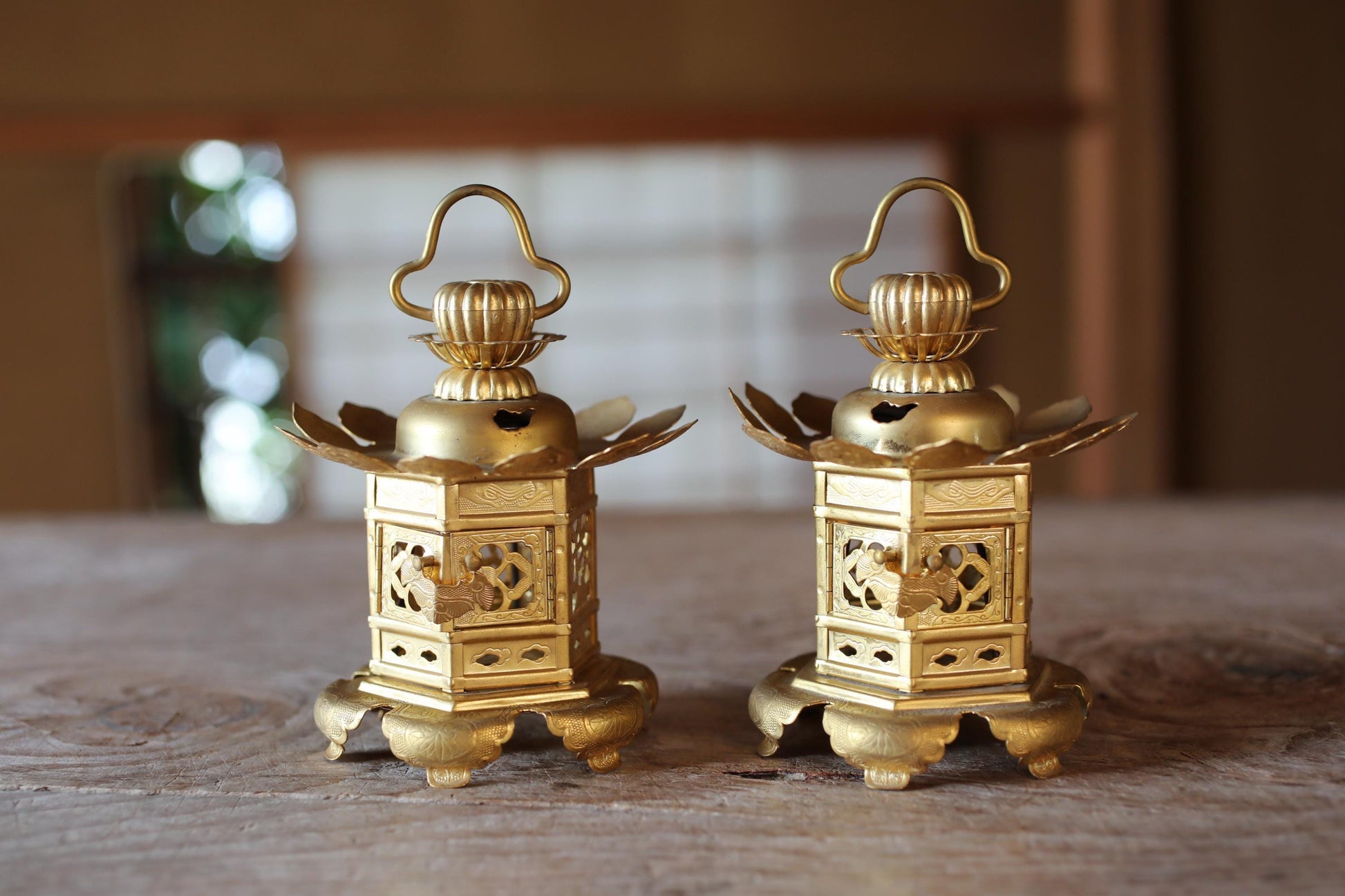 Two ornate gold lanterns with intricate designs are displayed on a wooden surface.