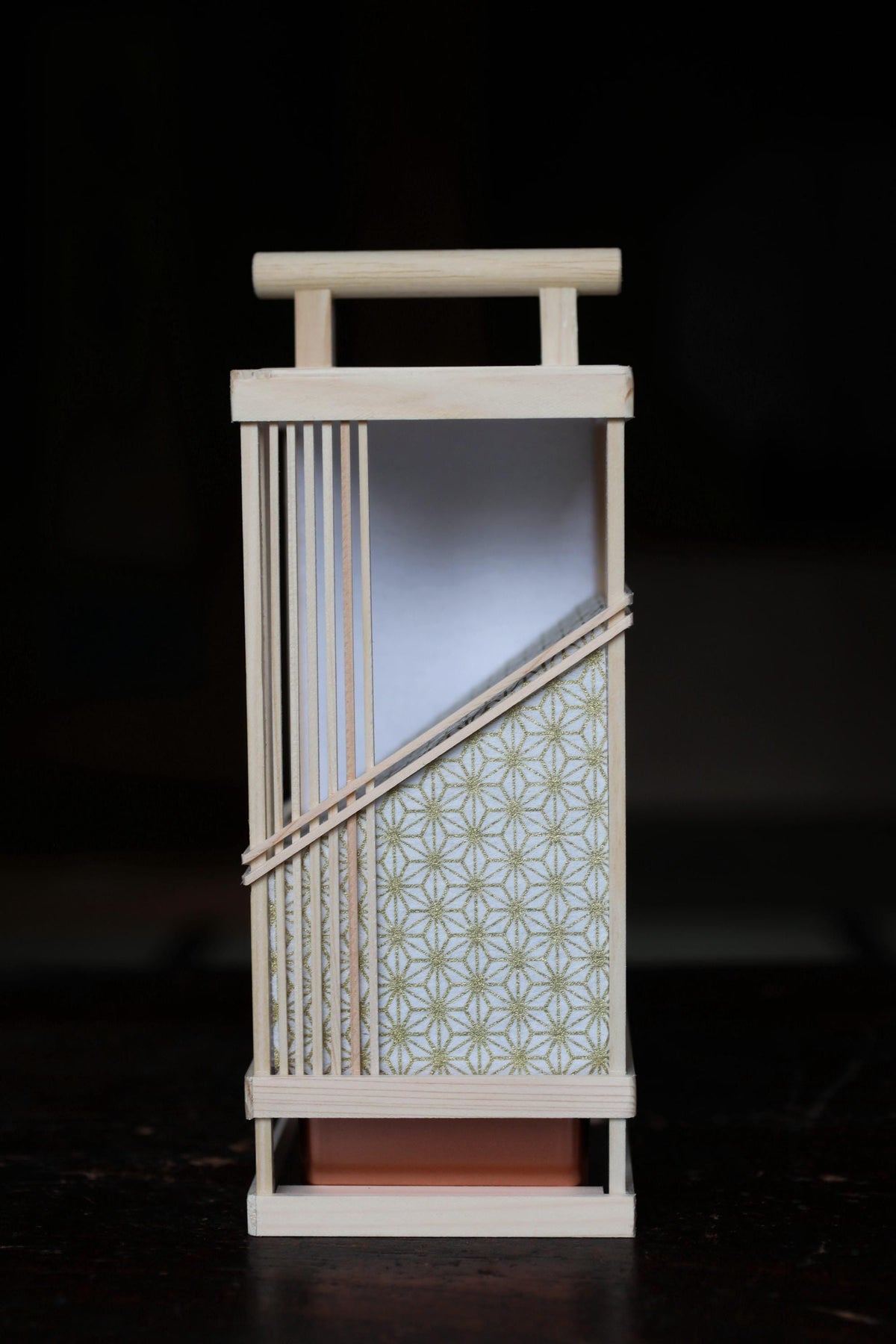A wooden lantern with a white interior and a patterned exterior, featuring a wooden handle and a wooden frame.
