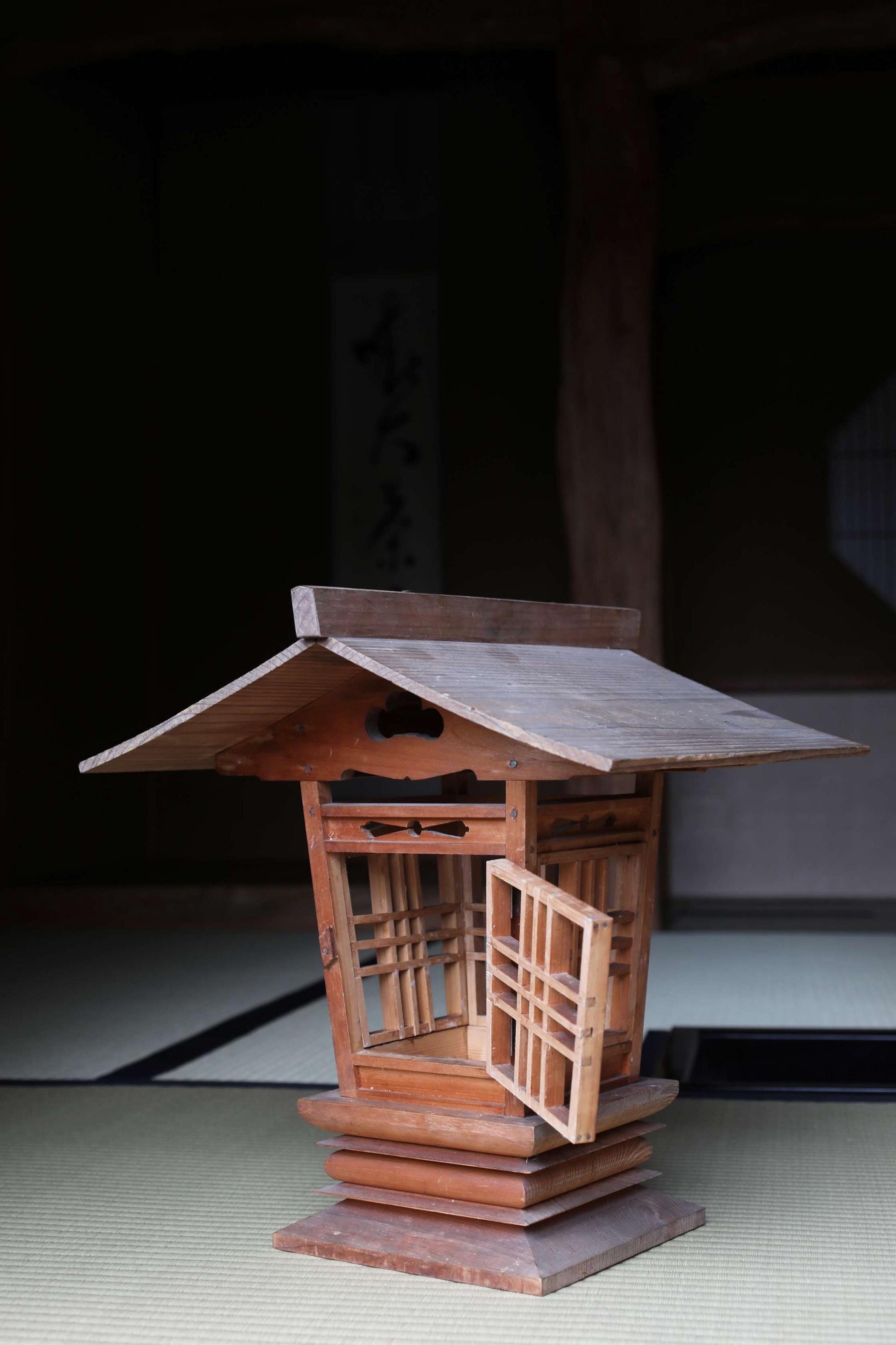 A wooden lantern with an open door, situated in a dimly lit room with a tatami mat on the floor.