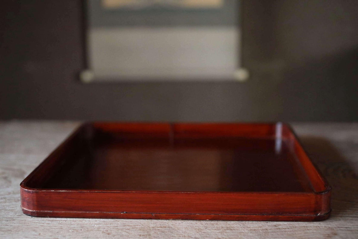 A wooden tray with a dark finish sits on a wooden surface.