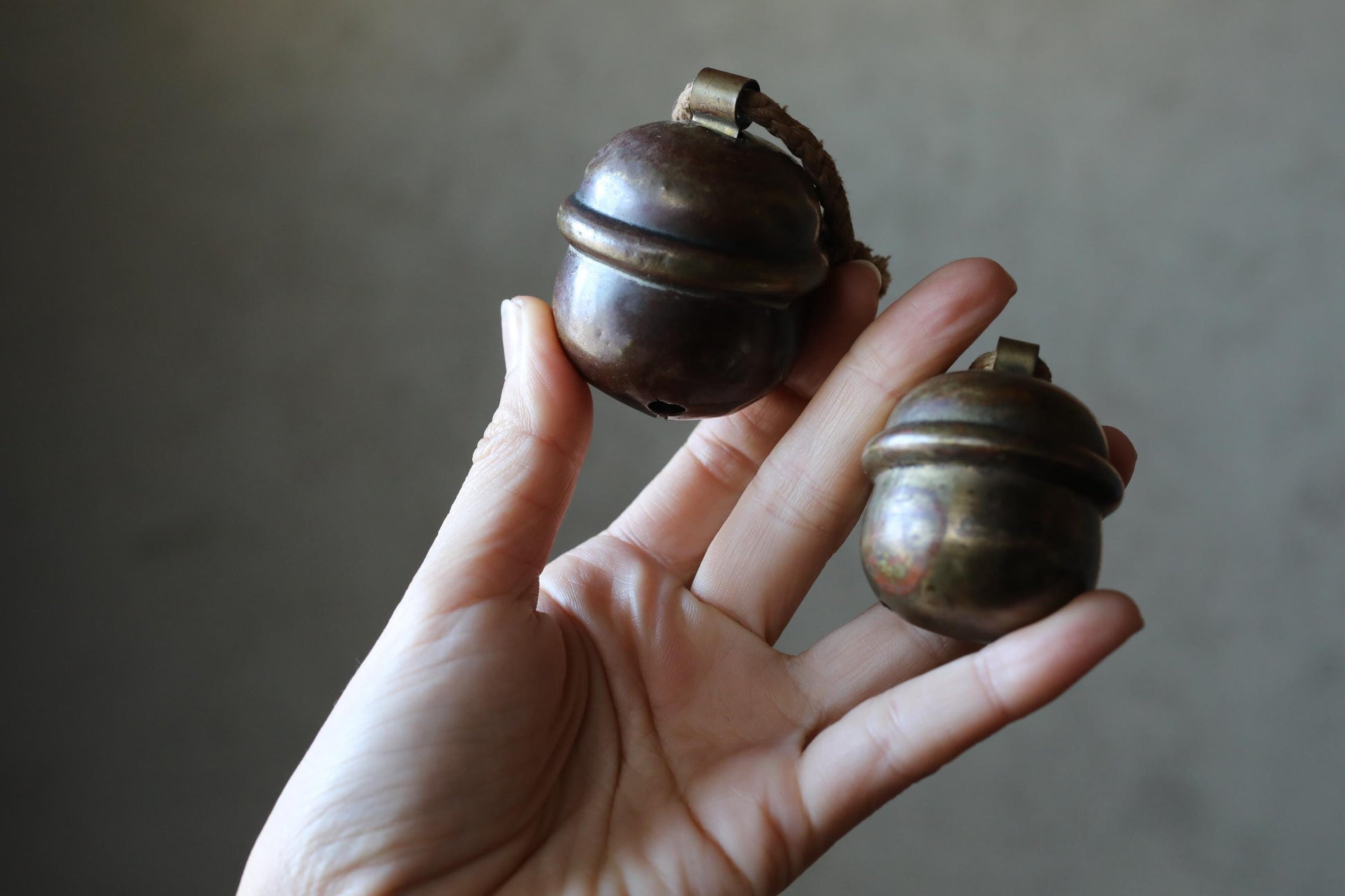 A hand holding two small, round brass bells.