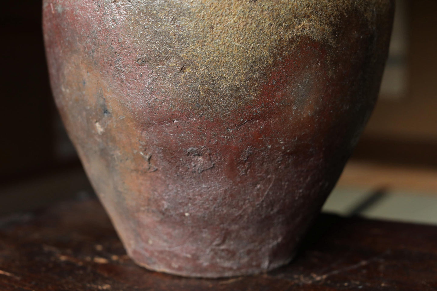 A close-up image of a weathered, rusted clay pot with a reddish-brown hue and visible cracks and chips on its surface.