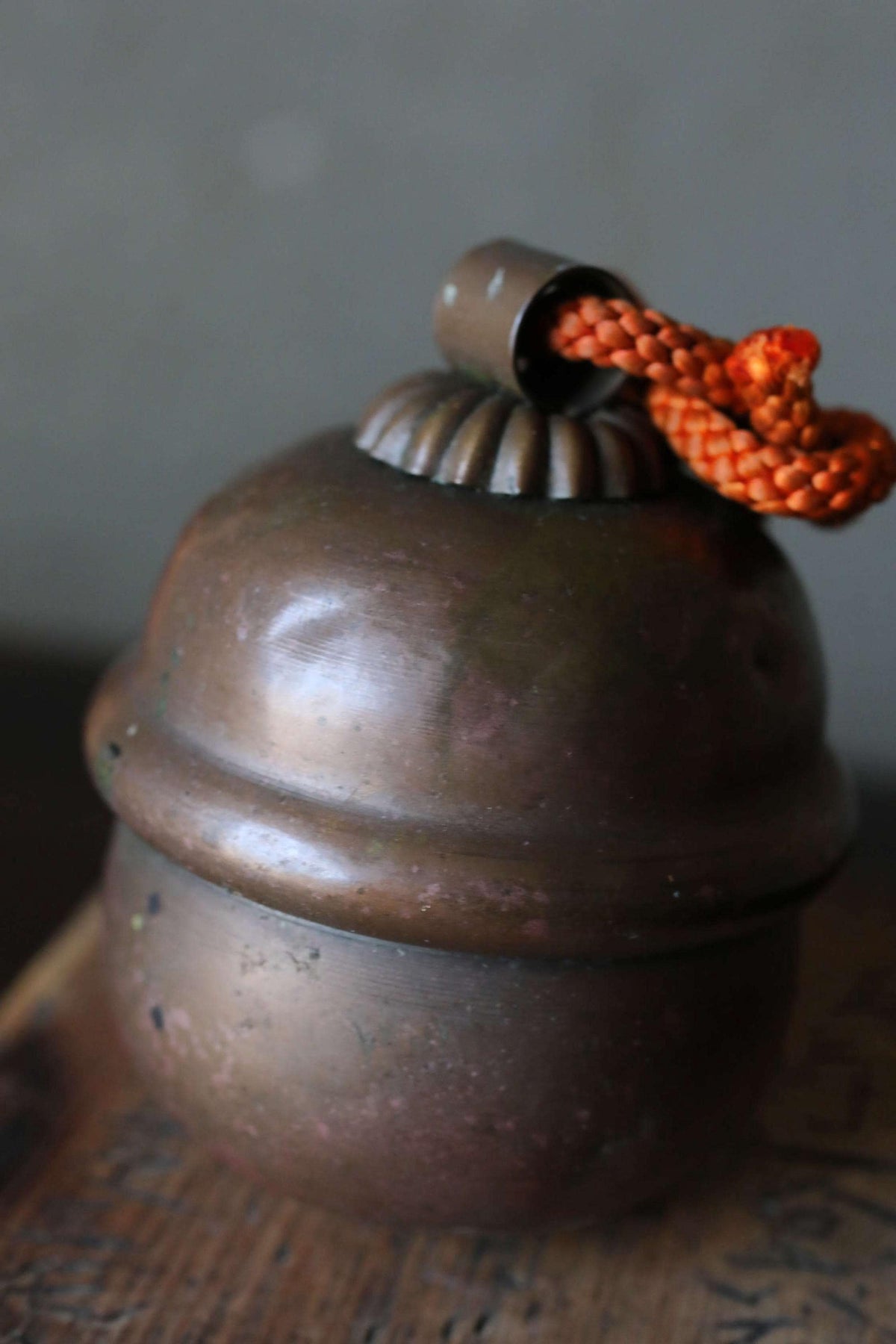 A close-up image of a round, metal object with a rope hanging from the top, resting on a wooden surface.