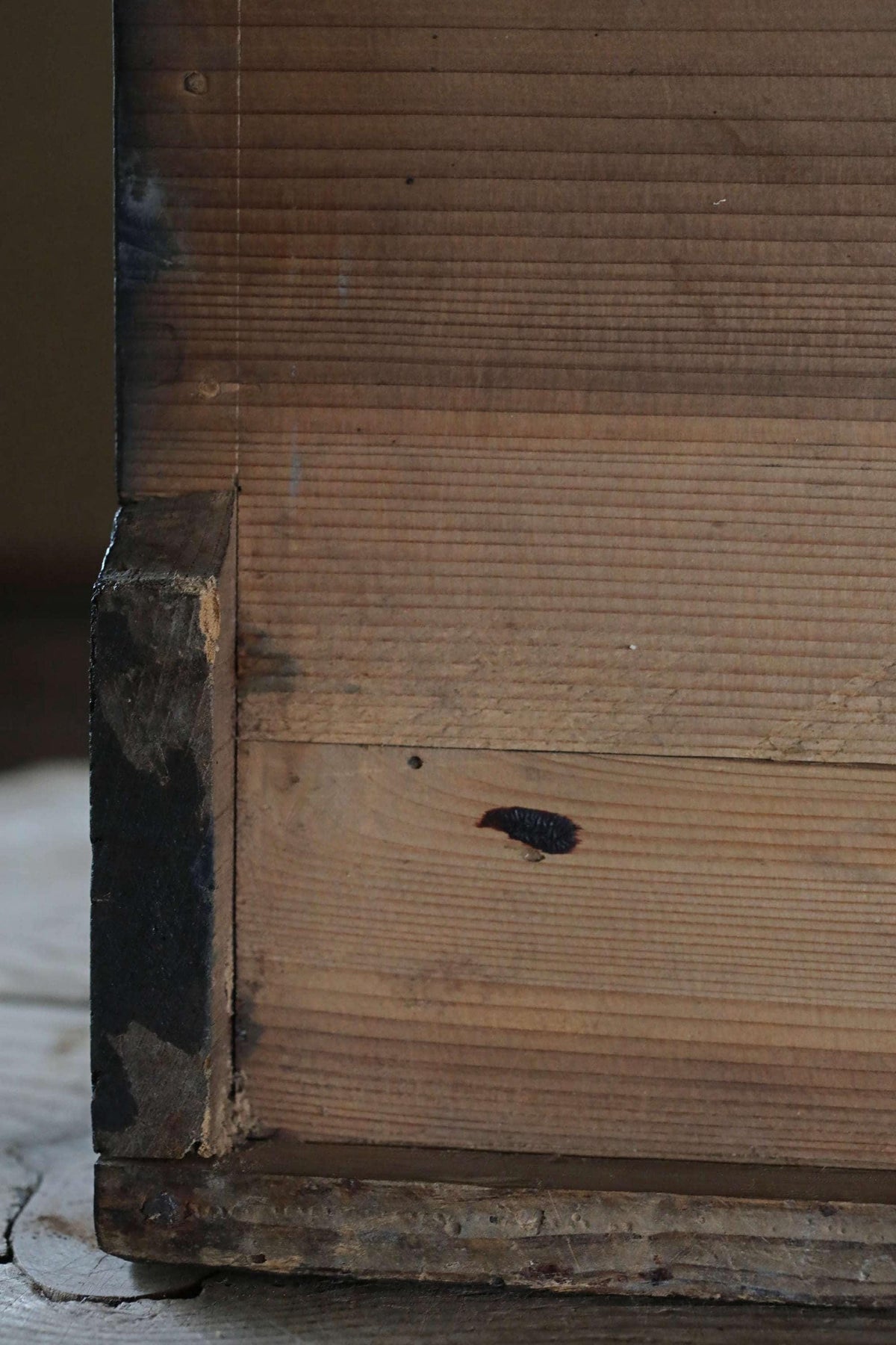 a close-up view of a wooden surface, possibly a piece of furniture or a wall, with visible signs of wear and tear, such as a small hole and some discoloration.