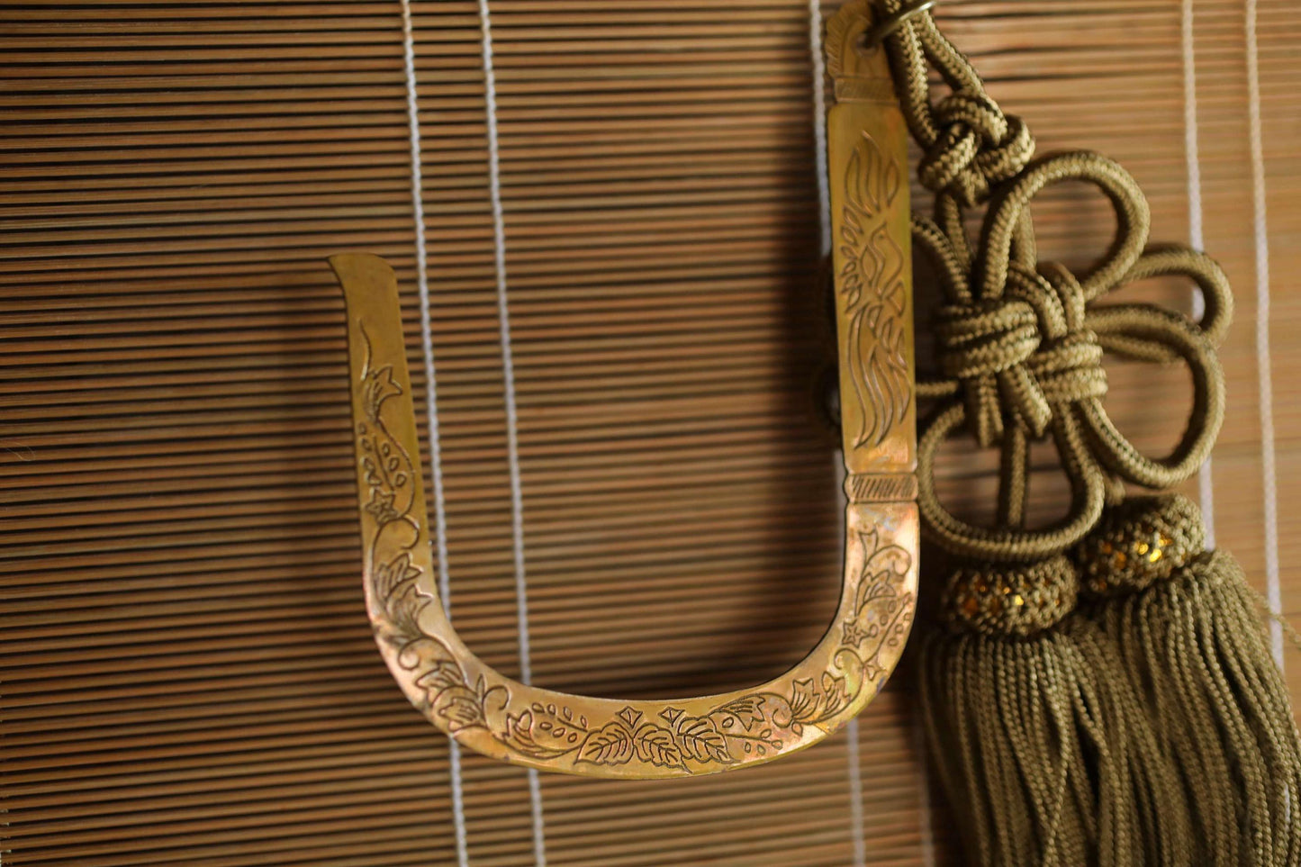 a decorative brass letter 'U' with intricate floral designs, hanging on a wooden blind.