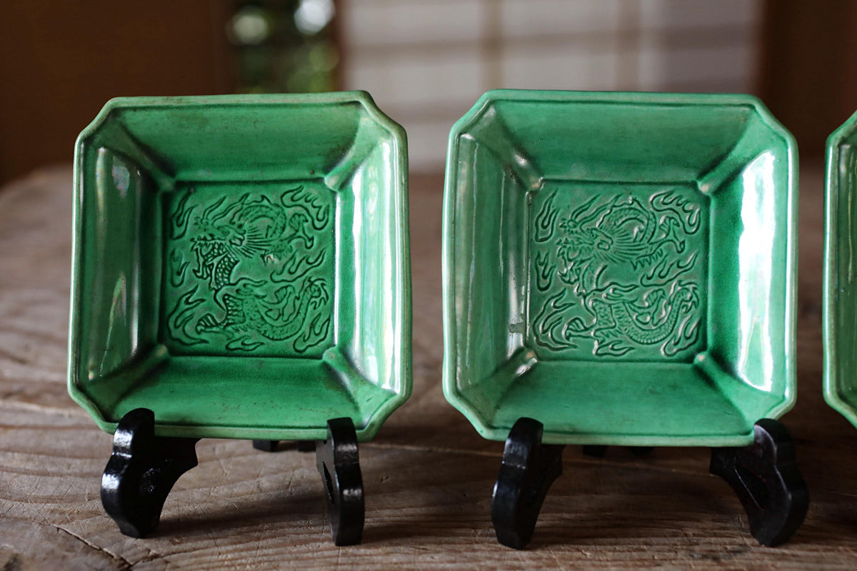 A pair of green ceramic plates with dragon designs, displayed on a wooden surface.