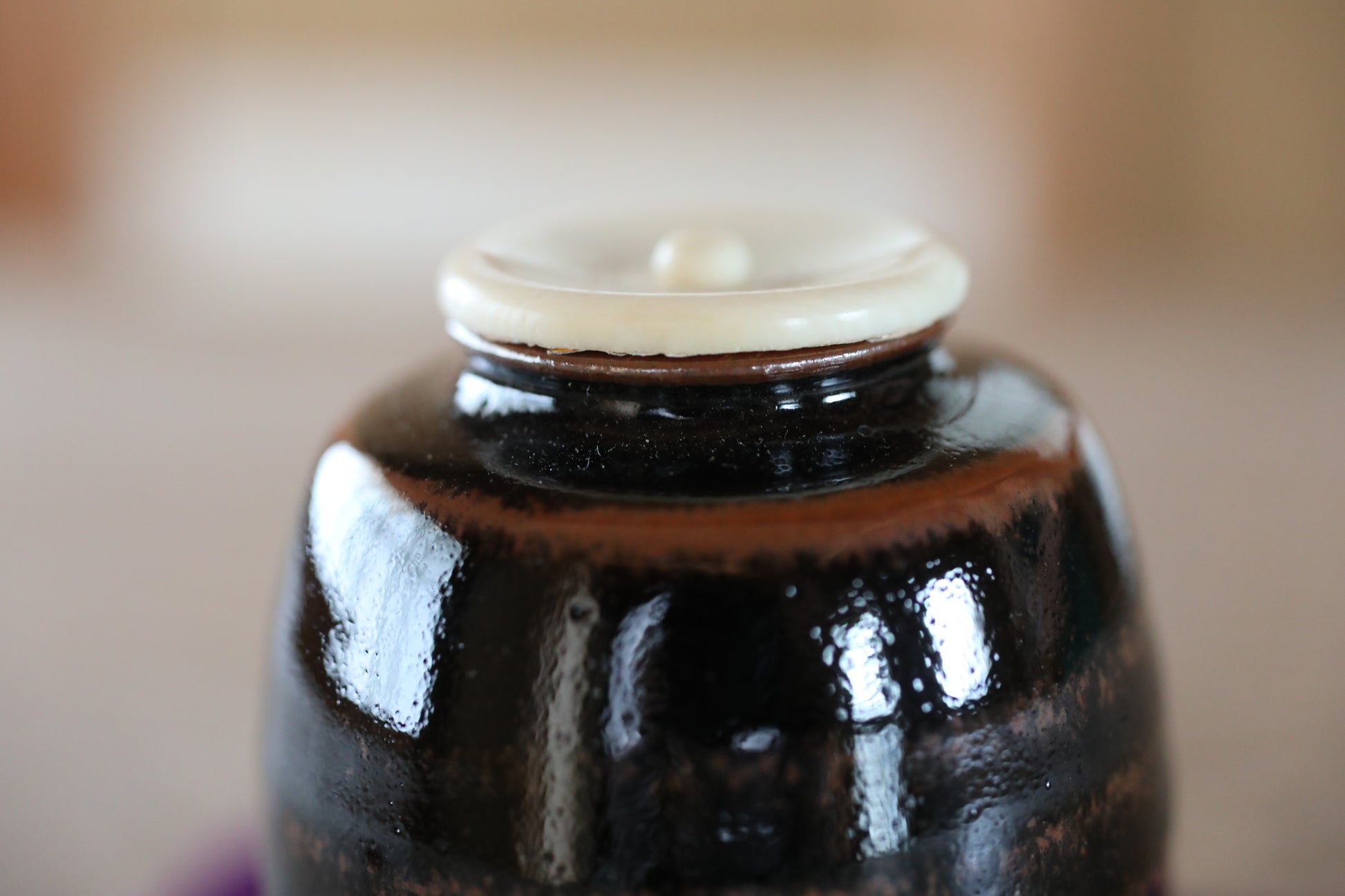 A close-up image of a dark brown ceramic jar with a white lid, placed on a surface.